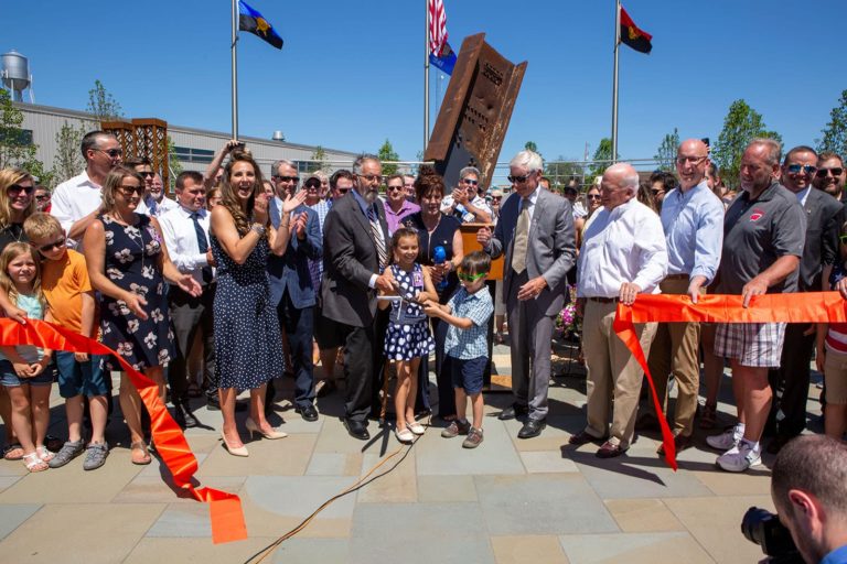 A group gathers in front of the Memorial steel to cut the ribbon and officially open the Memorial